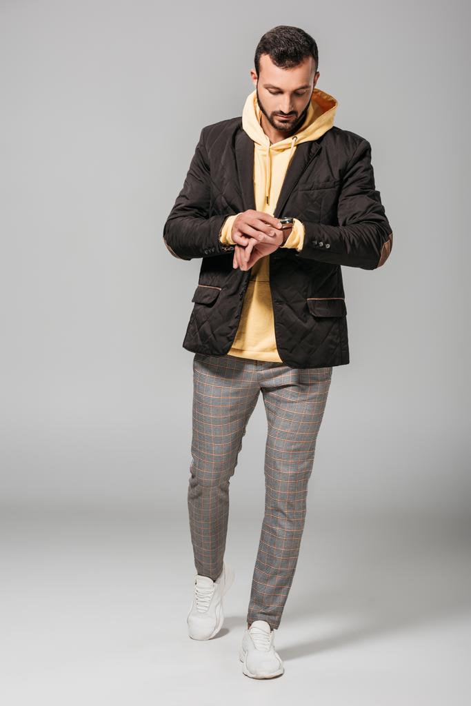 hombre joven de moda en traje de otoño mirando reloj de pulsera sobre fondo gris
  - Foto, Imagen