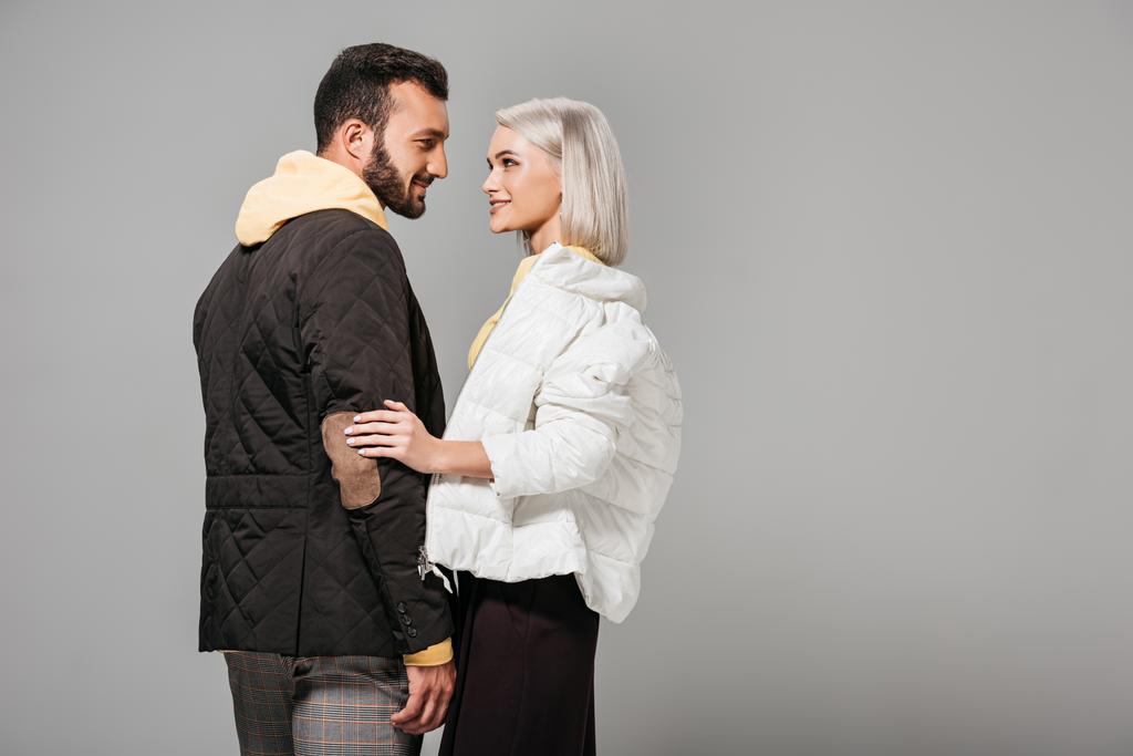 秋の服装を見てお互いに灰色の背景上で分離のモデルのスタイリッシュなカップルの側面図   - 写真・画像