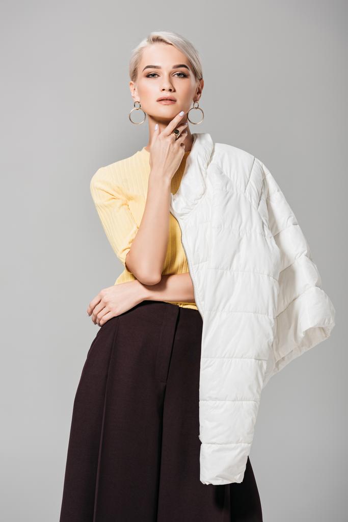 Κομψό γυναικείο μοντέλο ποζάρει με σακάκι πάνω από τον ώμο που απομονώνονται σε γκρι φόντο  - Φωτογραφία, εικόνα