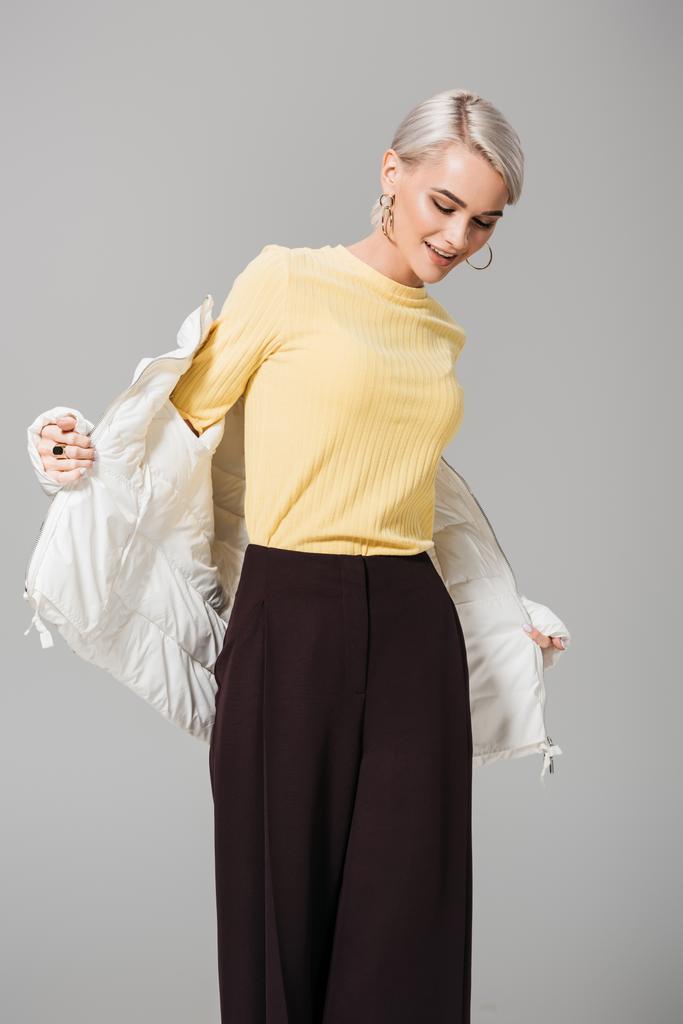 modelo feminino feliz colocando jaqueta de outono branco isolado no fundo cinza
  - Foto, Imagem