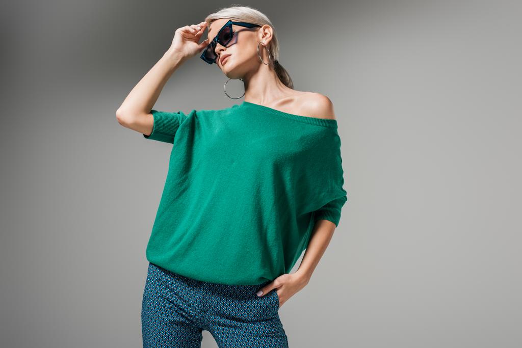 gyönyörű női modell, a napszemüveg és zöld pulóver jelentő elszigetelt szürke háttér  - Fotó, kép