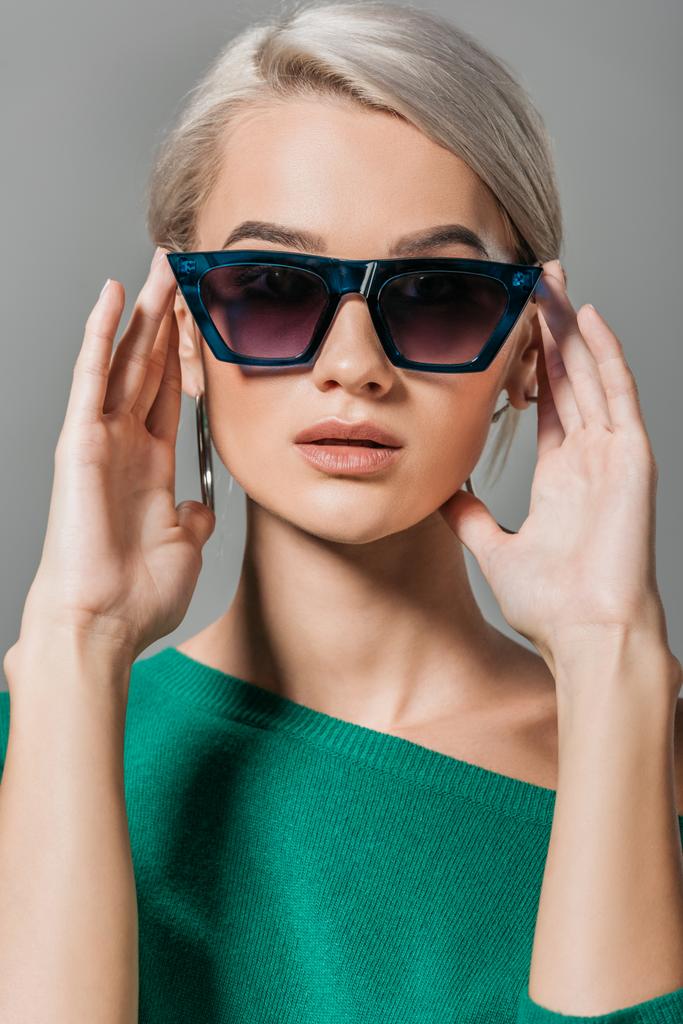 young stylish girl in sunglasses and green sweater looking at camera isolated on grey background  - Photo, Image
