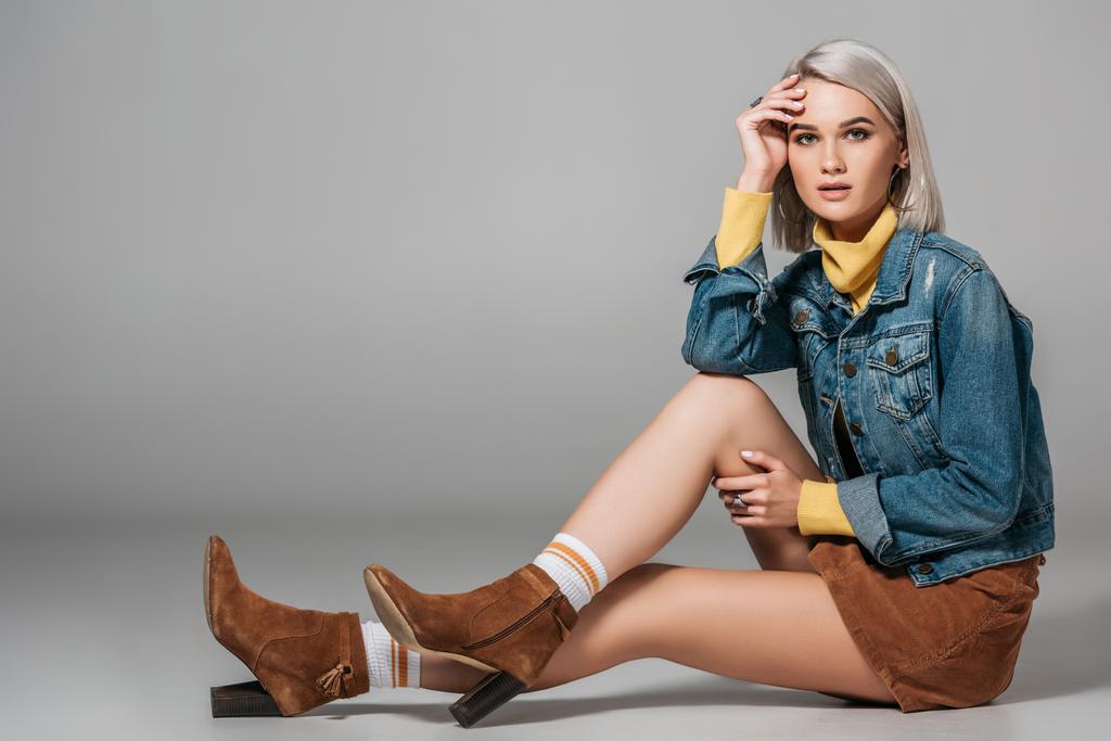 красивая модель в модной вельветовой юбке и джинсовой куртке, сидящая на полу, на сером
 - Фото, изображение