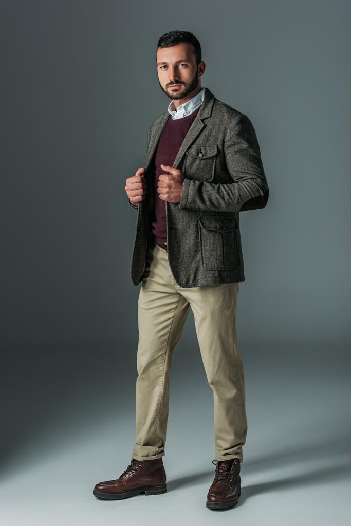 knappe mannelijke model poseren in beige broek en tweed jas, op grijs - Foto, afbeelding