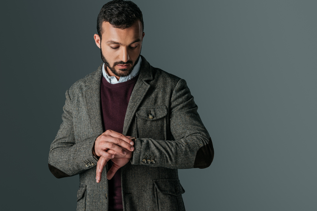Красивый мужчина в твидовом пиджаке, смотрящий на наручные часы, изолированные на сером
 - Фото, изображение