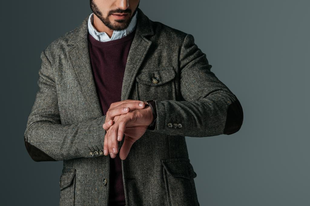 przycięte widzenia Brodaty mężczyzna w tweed kurtki, patrząc na zegarek, na szarym tle - Zdjęcie, obraz