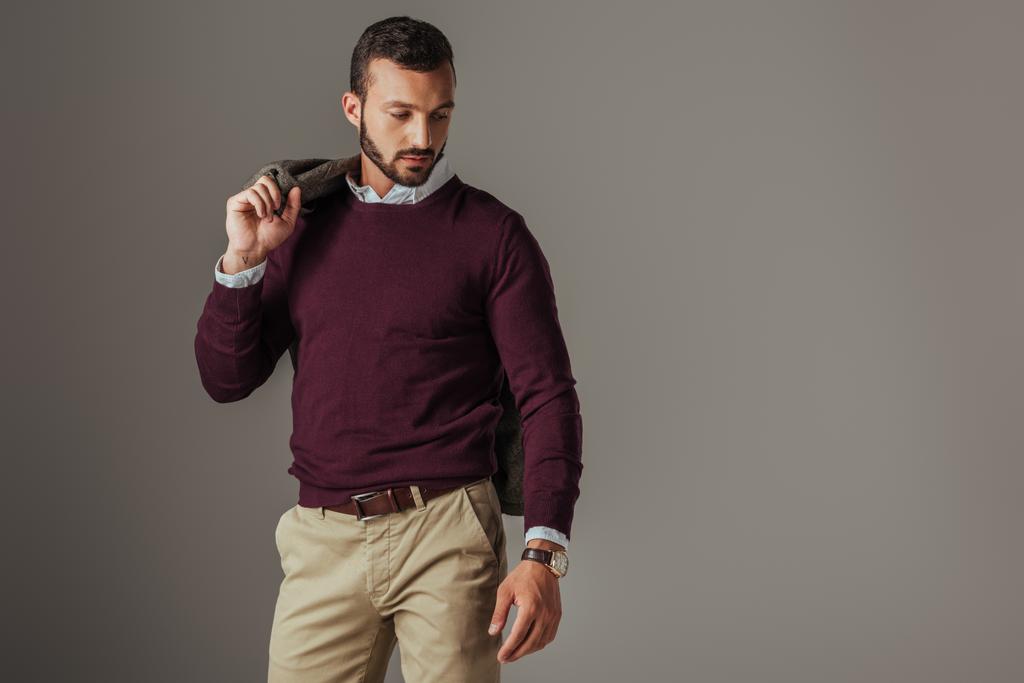 stylish handsome man posing in burgundy sweater with jacket on shoulder, isolated on grey - Photo, Image