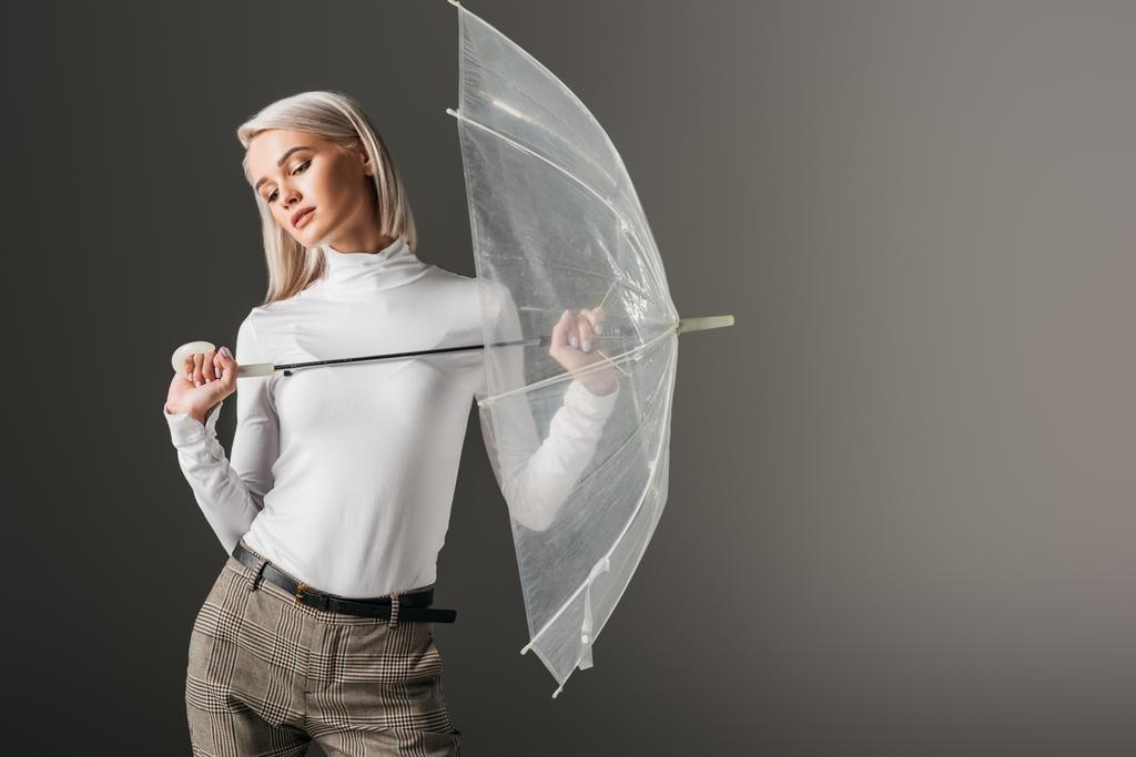 Nainen valkoisessa poolopaitaa poseeraa syksyllä läpinäkyvä sateenvarjo, eristetty harmaa
 - Valokuva, kuva
