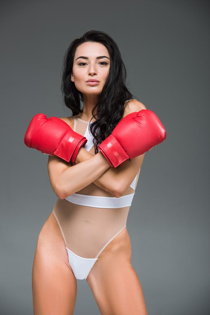 グレーに分離されたボクシング グローブで組んだ腕に白い水着立っている陽気な魅力的な女性 - 写真・画像