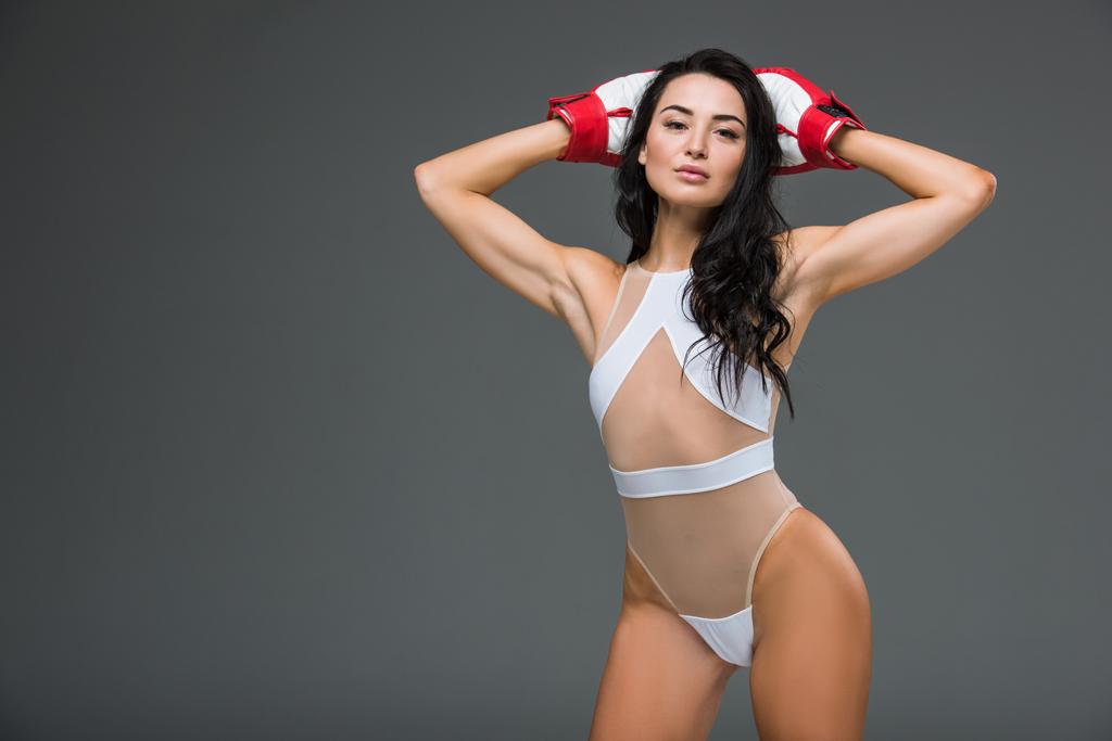 sexy donna sportiva in body bianco e guanti da boxe in piedi con le mani sopra la testa isolata sul grigio
 - Foto, immagini