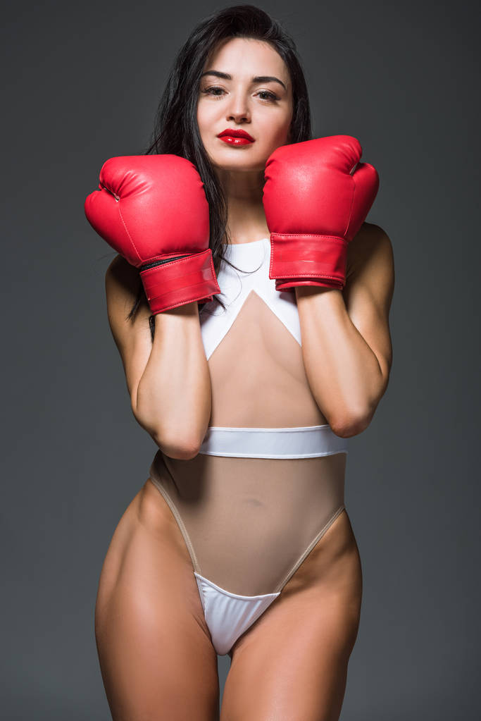 sexy donna sportiva in body bianco mostrando guanti da boxe rossi isolati su grigio
 - Foto, immagini