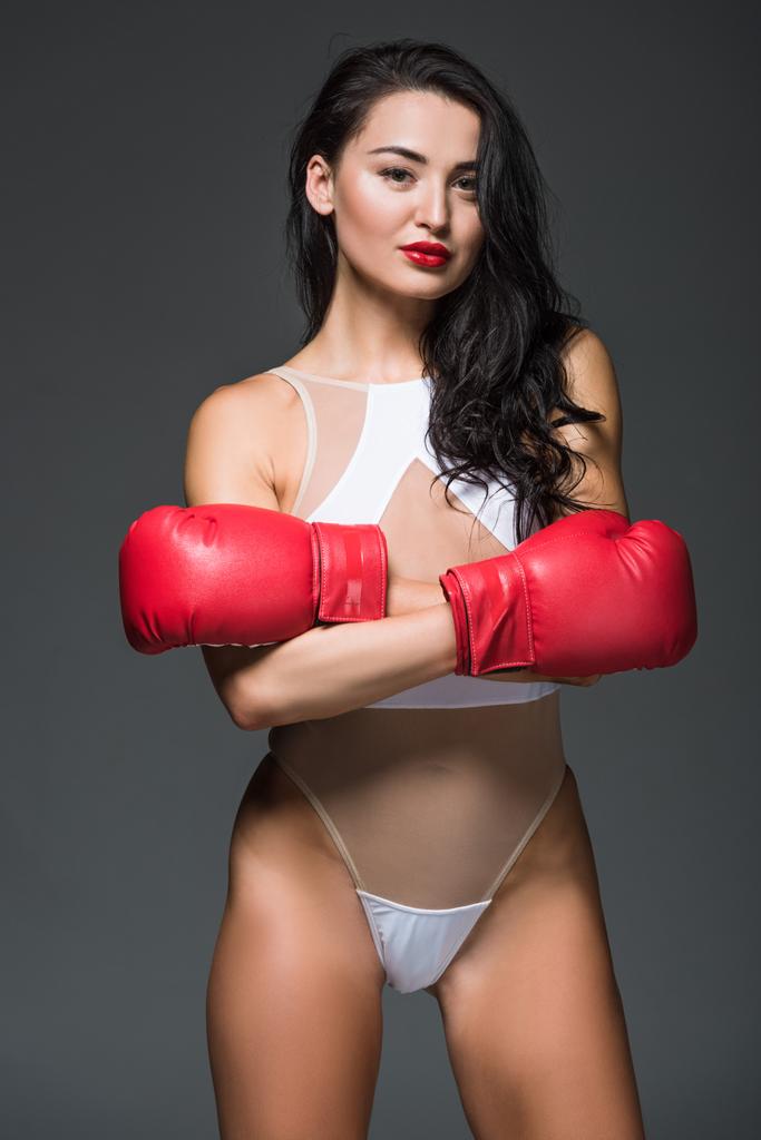seksikäs urheilullinen nainen valkoisissa urheiluvaatteissa ja nyrkkeilyhanskat seisoo ristissä kädet eristetty harmaa
  - Valokuva, kuva