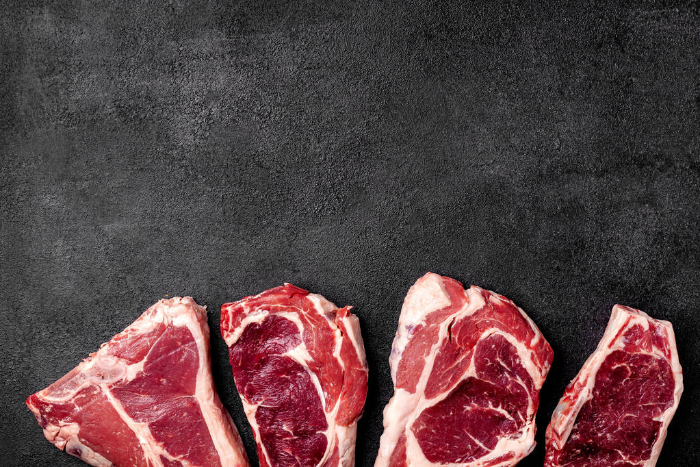 Κρέας νωπό μπριζόλα βρίσκεται σε μαύρο φόντο. Πλάγια όψη, διάστημα αντίγραφο, το top view - Φωτογραφία, εικόνα