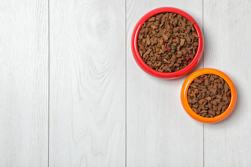 Tigelas com comida para gato e cachorro em fundo de madeira. Cuidados com animais
 - Foto, Imagem