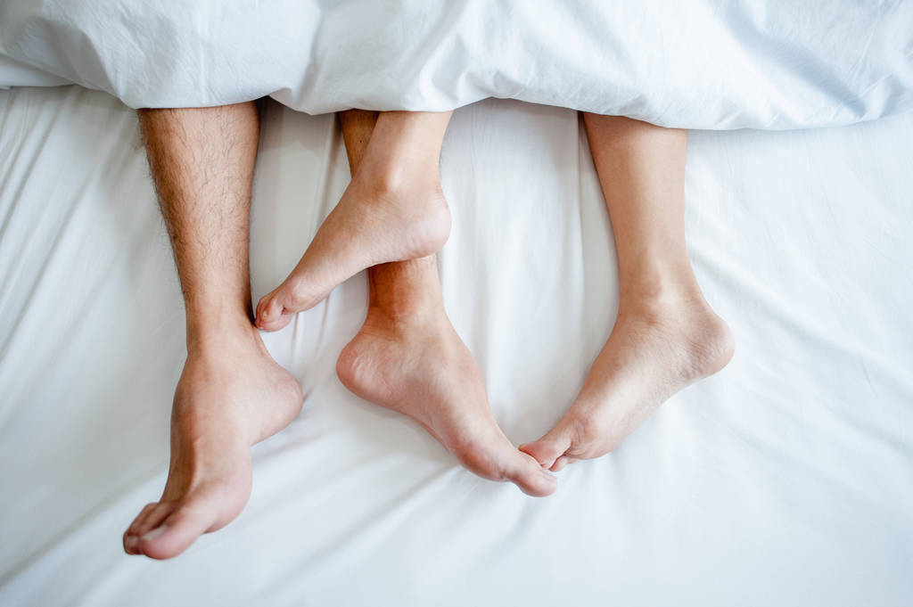 Amore sdraiato a letto in hotel, abbracciato su lenzuola bianche, gambe vicine. - Foto, immagini