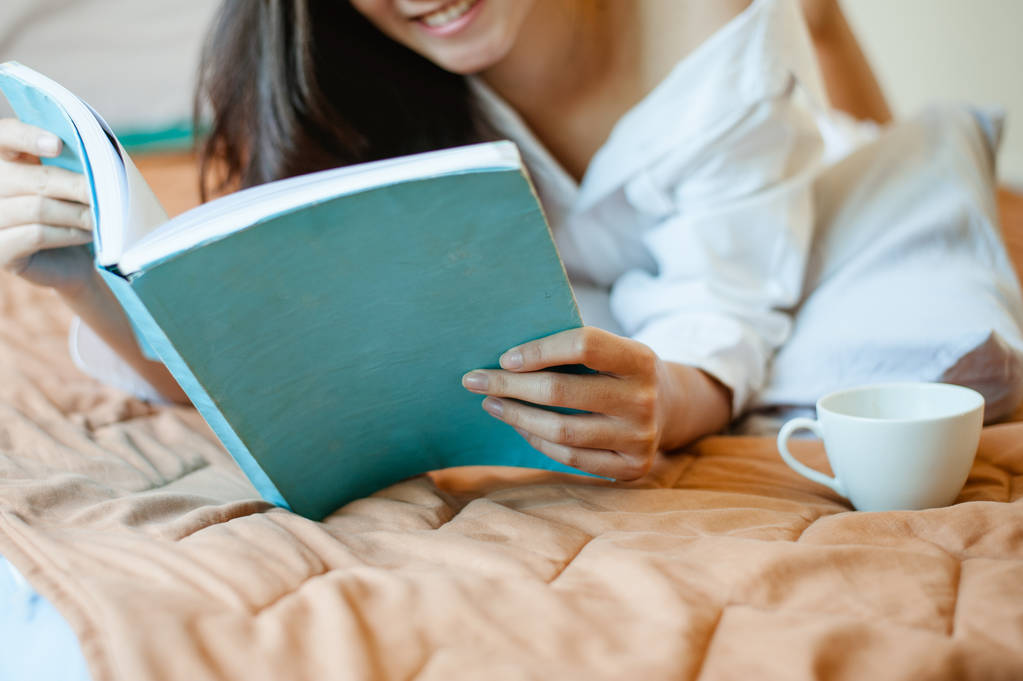  vrouw die boek leest en koffie drinkt op bed. - Foto, afbeelding