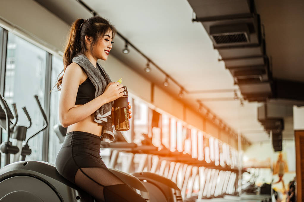 Jeune femme en forme fatiguée de boire de la boisson protéinée en salle de gymnastique. - Photo, image