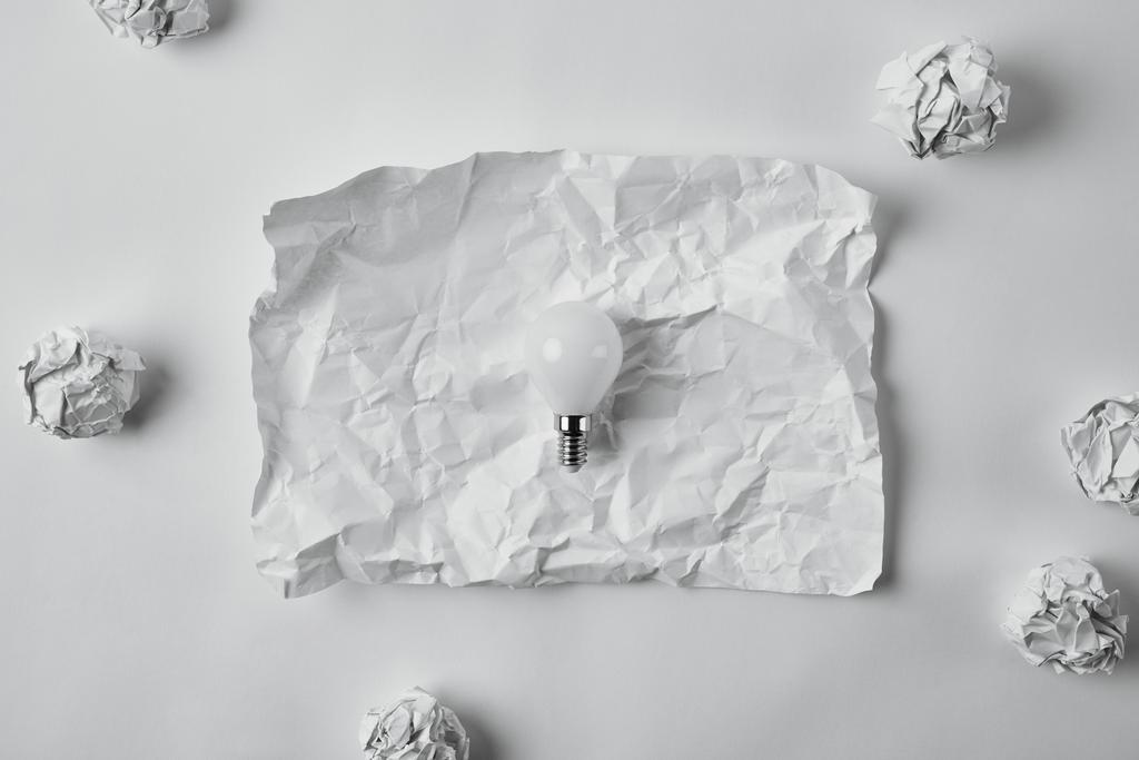 κάτοψη της εξοικονόμησης ενέργειας λάμπα στο τσαλακωμένο χαρτί κενό σε λευκή επιφάνεια - Φωτογραφία, εικόνα