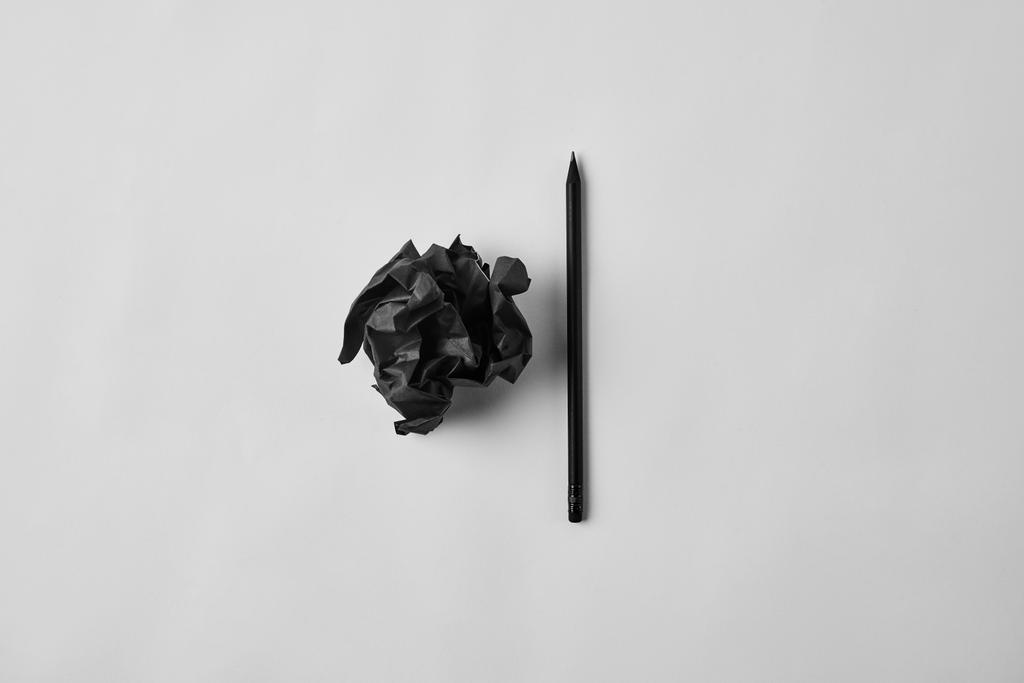 zwarte verfrommeld papier met potlood op wit oppervlak (bovenaanzicht) - Foto, afbeelding