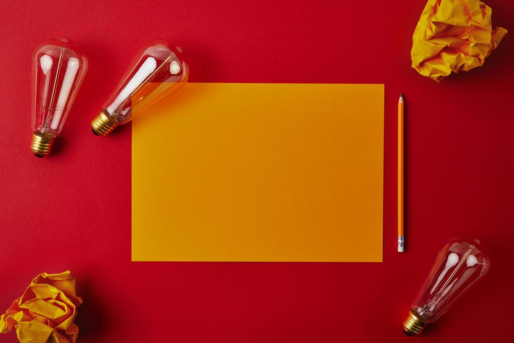 vista superior de papel blanco amarillo con papeles arrugados y lámparas incandescentes sobre superficie roja
 - Foto, Imagen