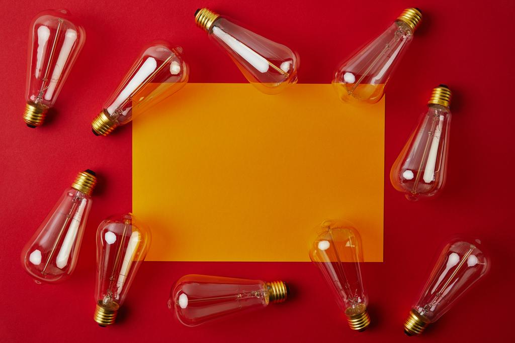 Ansicht von Vintage-Glühlampen auf roter Oberfläche mit gelbem Blankopapier - Foto, Bild