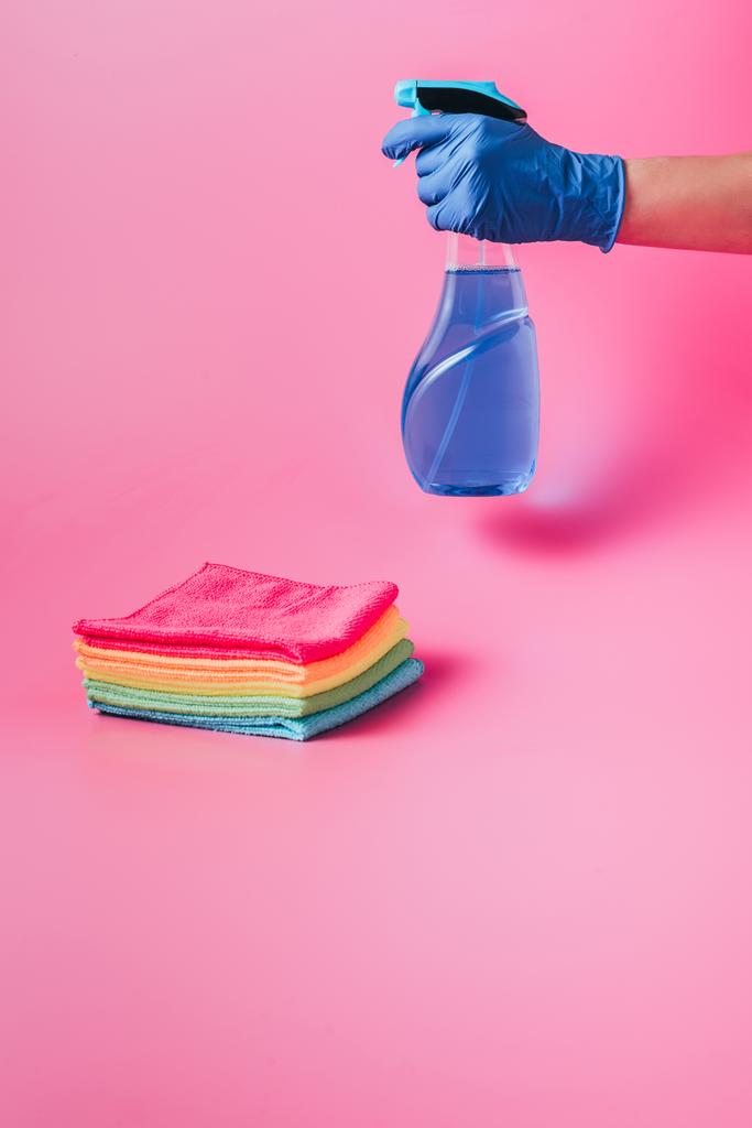 ořízne obraz žena čisticí drží čisticí kapaliny v blízkosti zásobníku barevné hadry, růžové pozadí - Fotografie, Obrázek