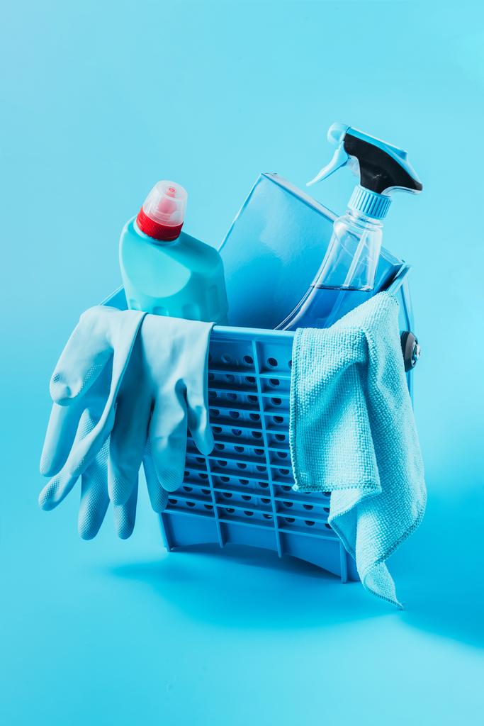 close up view of bucket with washing powder, cleaning fluids, rubber gloves and rag on blue background  - Photo, Image