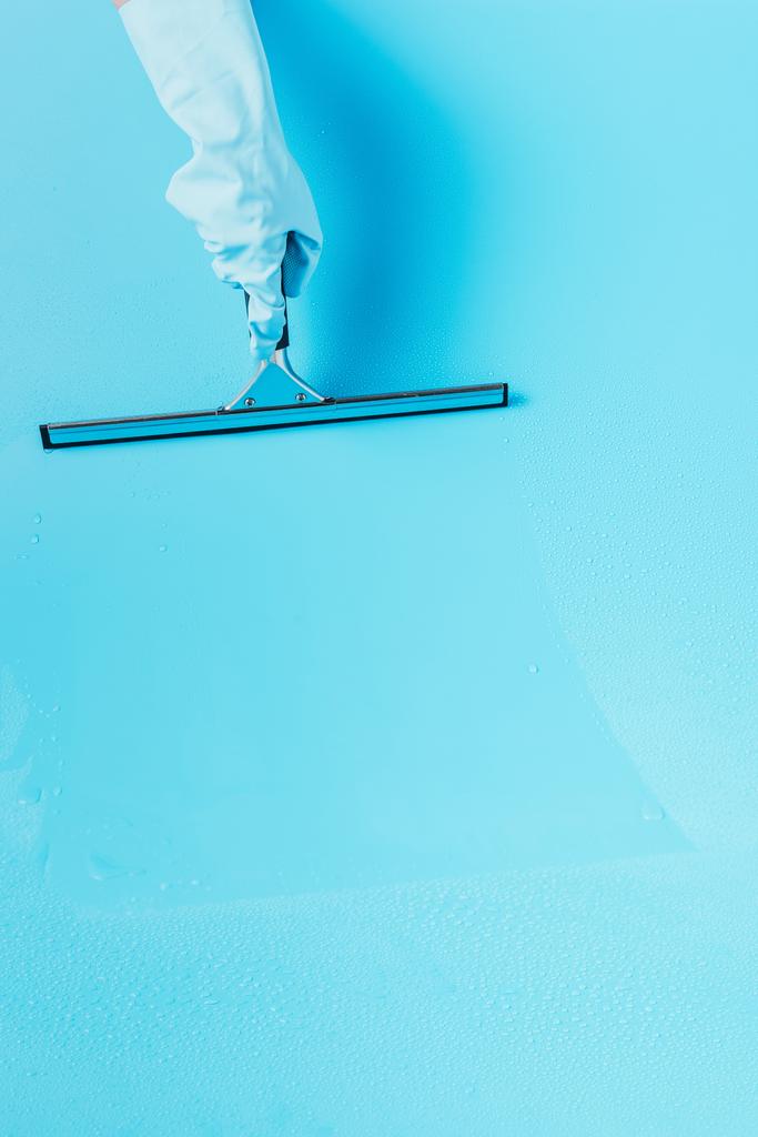 bijgesneden afbeelding van vrouw in rubberen handschoen vloer schoonmaken door zuigmond, blauwe achtergrond - Foto, afbeelding