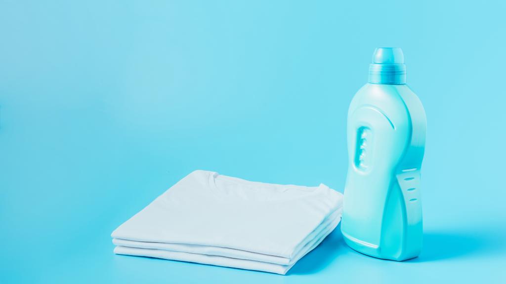 vista de cerca del líquido de lavandería y pila de camisetas blancas limpias, fondo azul
  - Foto, Imagen