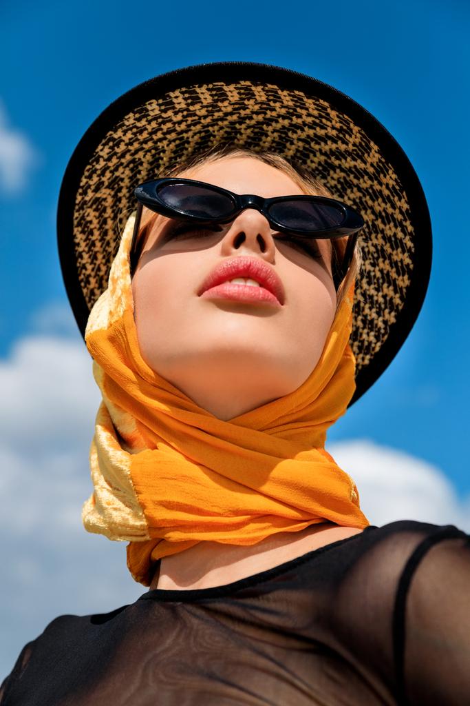 Blick von unten auf stilvolles Mädchen mit trendiger Sonnenbrille und Hut - Foto, Bild