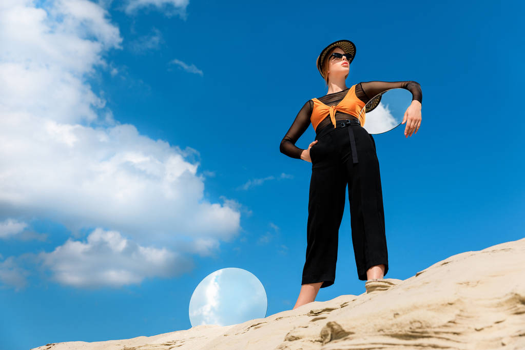 элегантная красивая модель в стильной одежде с круглыми зеркалами с отражением облачного неба
 - Фото, изображение