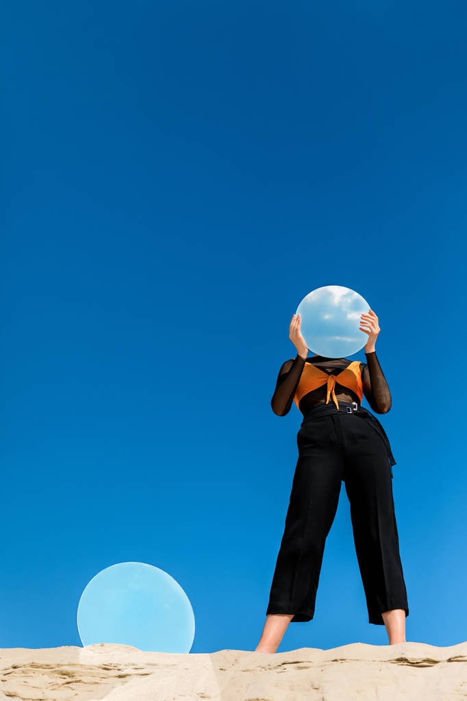 модная модель, держащая зеркало с отражением неба перед лицом
 - Фото, изображение