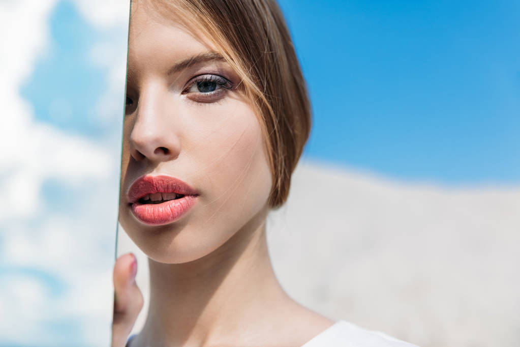 jonge mooie vrouw poseren met spiegel met reflectie voor sky  - Foto, afbeelding