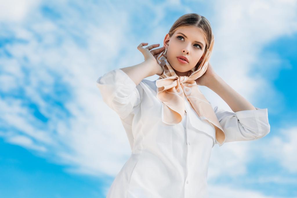 вид снизу красивой стильной женщины в белой одежде и шелковом шарфе, с голубым облачным небом
 - Фото, изображение