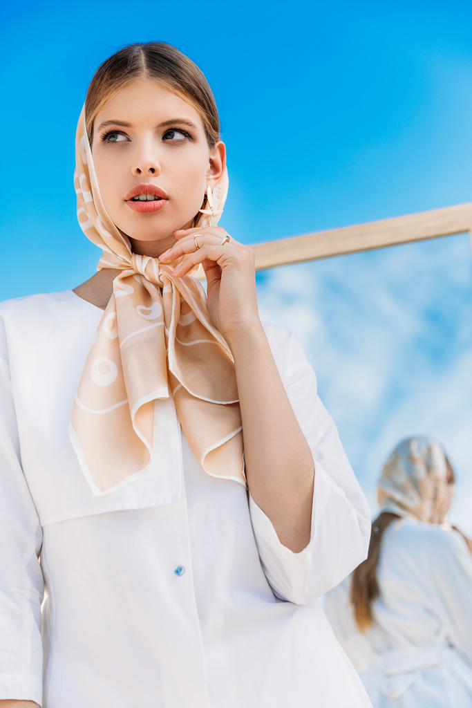 modieuze vrouw poseren in witte kleren en zijden sjaal in de buurt van spiegel  - Foto, afbeelding