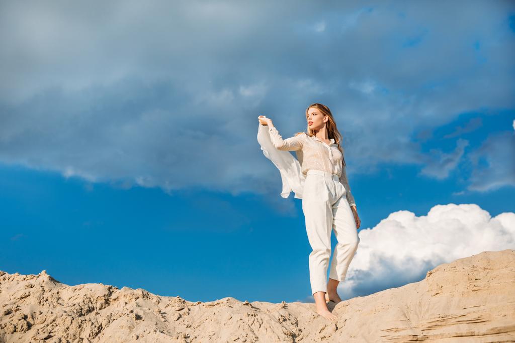 charmant modèle à la mode en vêtements blancs à la mode avec foulard en soie marchant sur une dune de sable
 - Photo, image