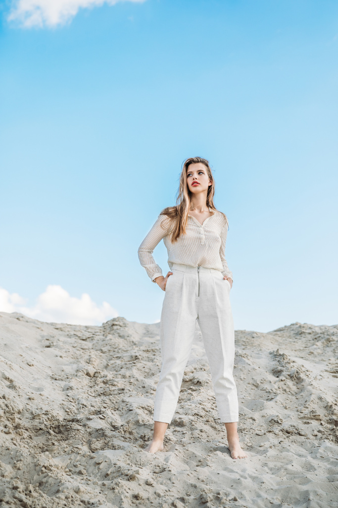 houkutteleva muodikas nainen valkoisissa vaatteissa poseeraa hiekkadyyni
 - Valokuva, kuva