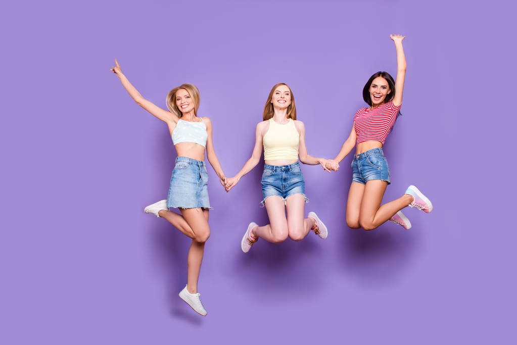 Портрет глупых игривых девушек, держащихся за руки, прыгающих в воздухе, наслаждающихся отпуском, празднуя достижение, изолированное на ярком фиолетовом фоне
 - Фото, изображение