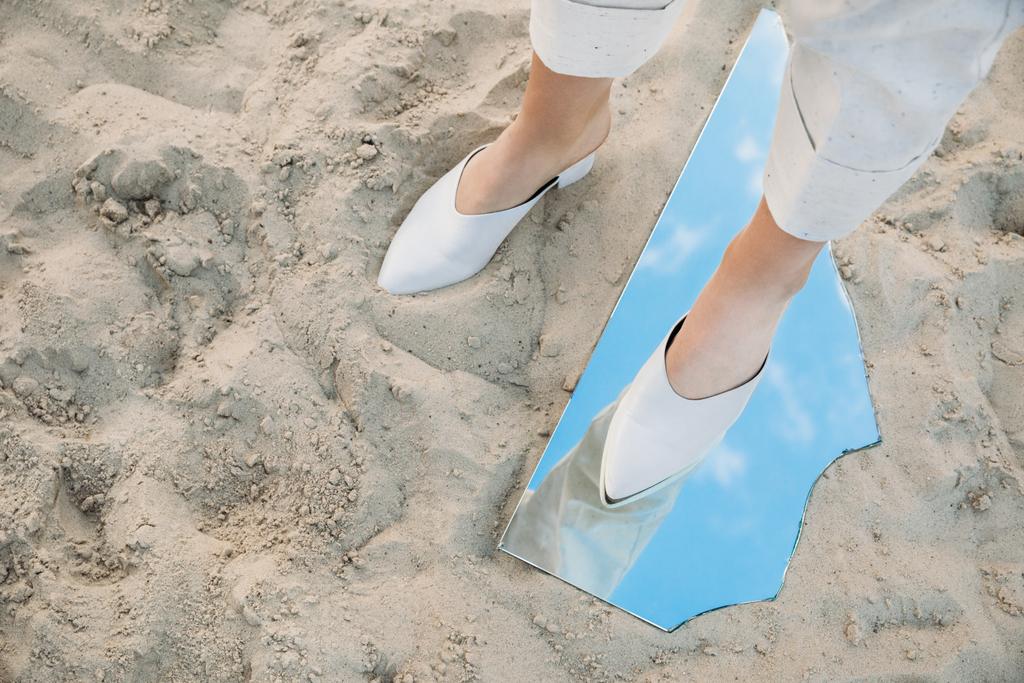 gedeeltelijke weergave van model staande op zand en stuk van spiegel met reflectie van de blauwe hemel - Foto, afbeelding