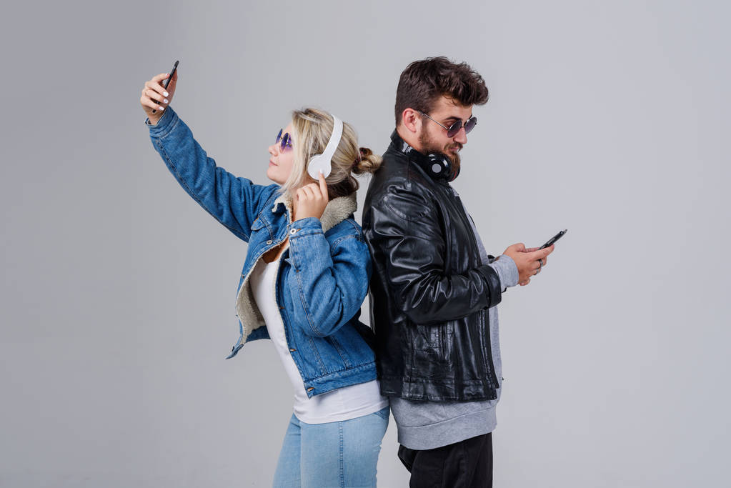 Portrait d'un jeune couple jouissant de musique et faisant du selfie sur fond gris
 - Photo, image