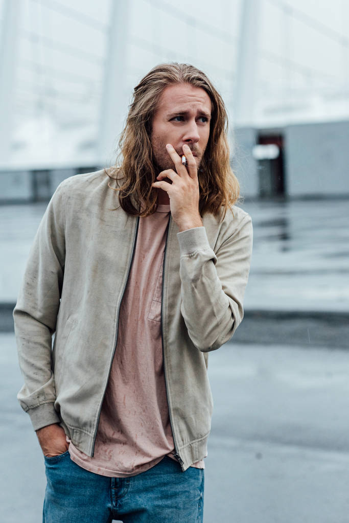 attraktiver junger Mann raucht an bewölkten Tagen Zigarette auf der Straße - Foto, Bild