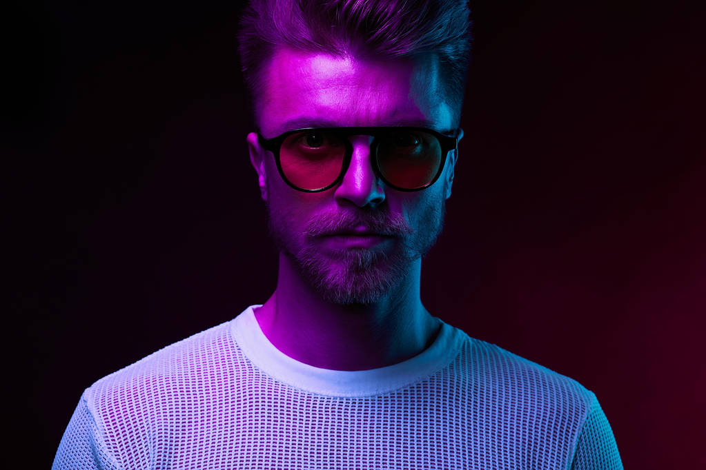 Neon light portrait of serious man model with mustaches and beard in sunglasses and white t-shirt  - Photo, Image