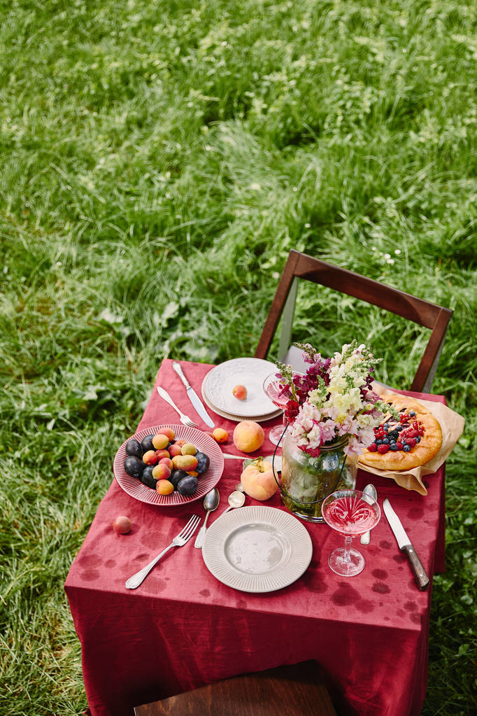 high angle view of table with fruits, pie and flowers in garden - Photo, Image