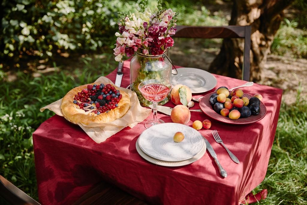 Weinglas, Beerenkuchen und Früchte auf dem Tisch im Garten - Foto, Bild