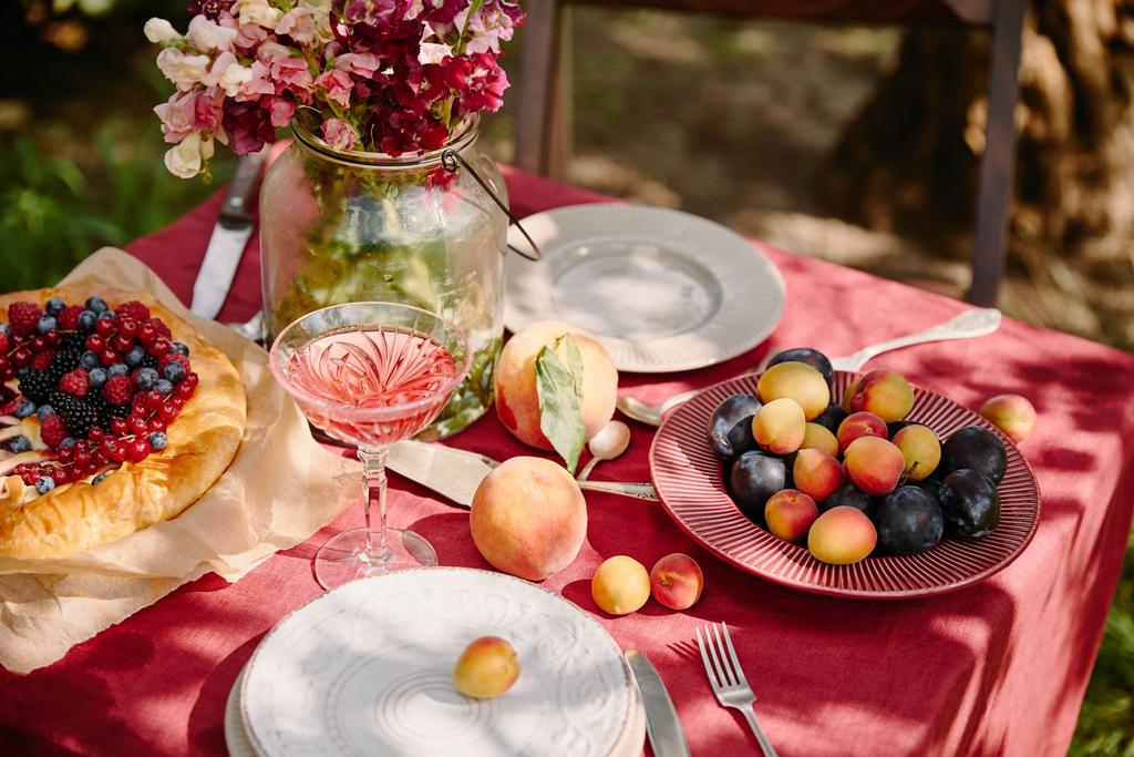 rijpe vruchten, wijnglas en boeket bloemen op tafel in de tuin - Foto, afbeelding