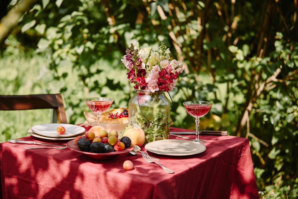 fruits, wineglasses and bouquet of flowers on table in garden - Photo, Image