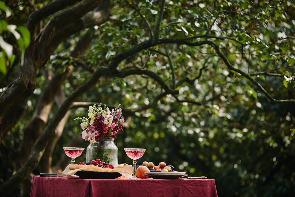 bouquet di fiori in vaso di vetro e bicchieri da vino sul tavolo in giardino verde
 - Foto, immagini