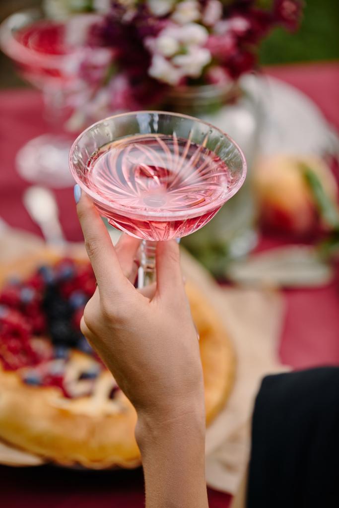 oříznutý obraz ženy držící Sklenka růžového vína u stolu v zahradě - Fotografie, Obrázek