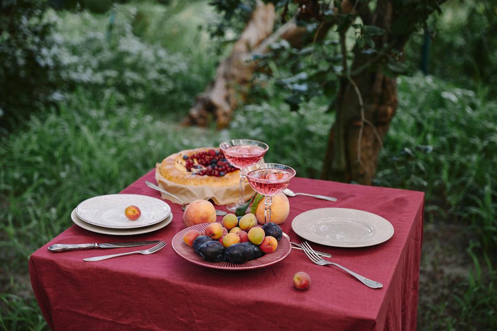 Weingläser, Beerenkuchen, Teller und Früchte auf dem Tisch im Garten - Foto, Bild