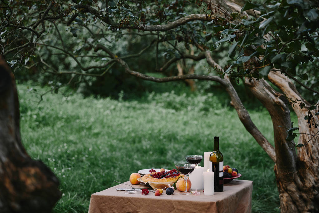 candles, glasses with wine and pie on table in garden - Photo, Image